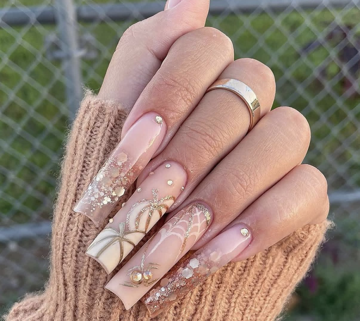 Long nude nails with gold bows, glitter and crystal accents